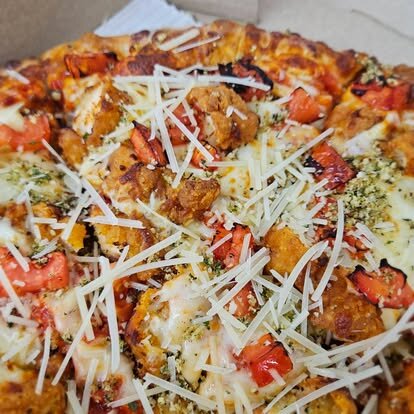 Chicken parmesan pizza topped with tomatoes and shaved parmesan